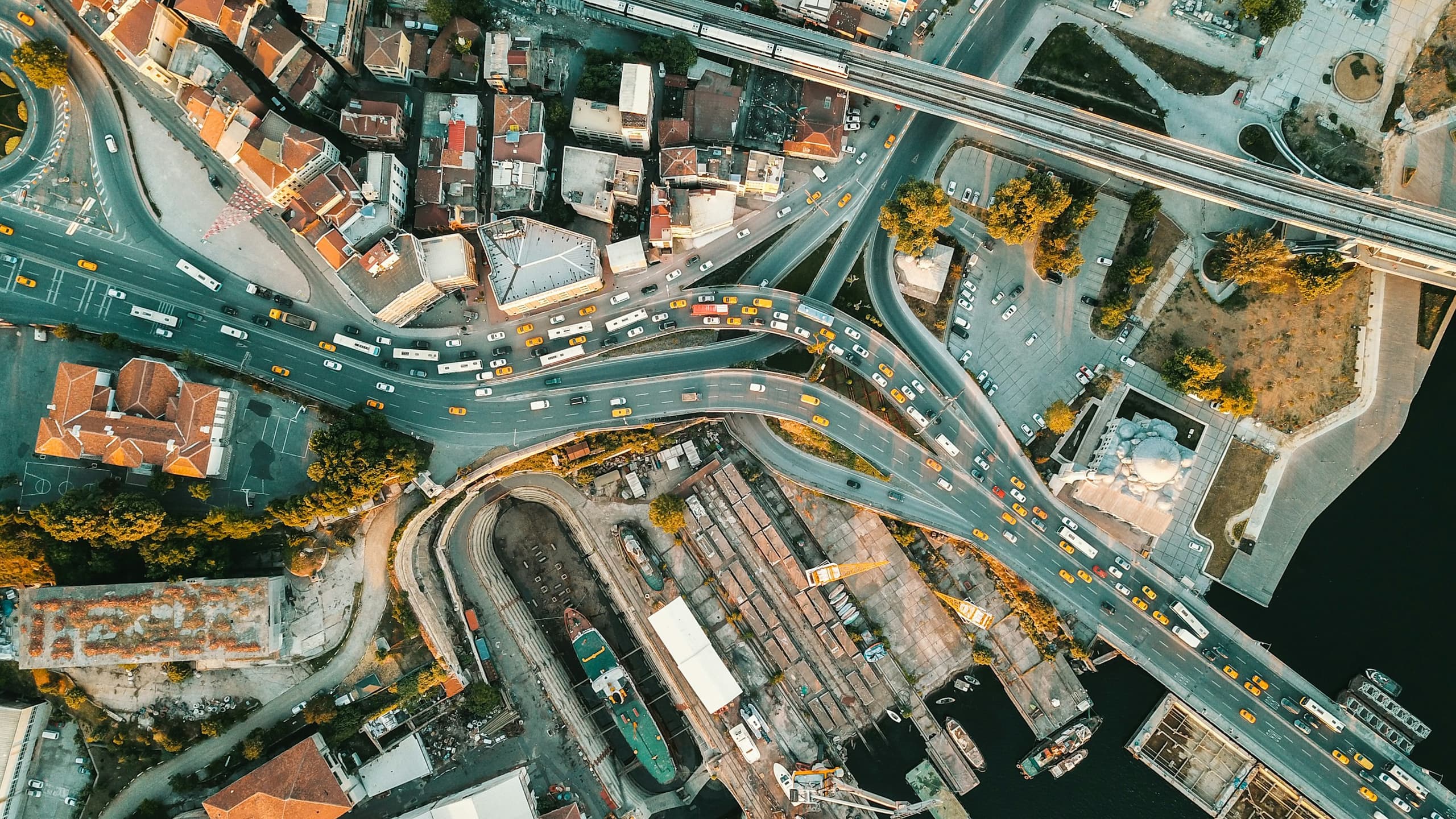 Near-vertical aerial view of Şişhane, İstanbul: road interchanges, rail lines, buses and dense older blocks running down to the Golden Horn waterfront.