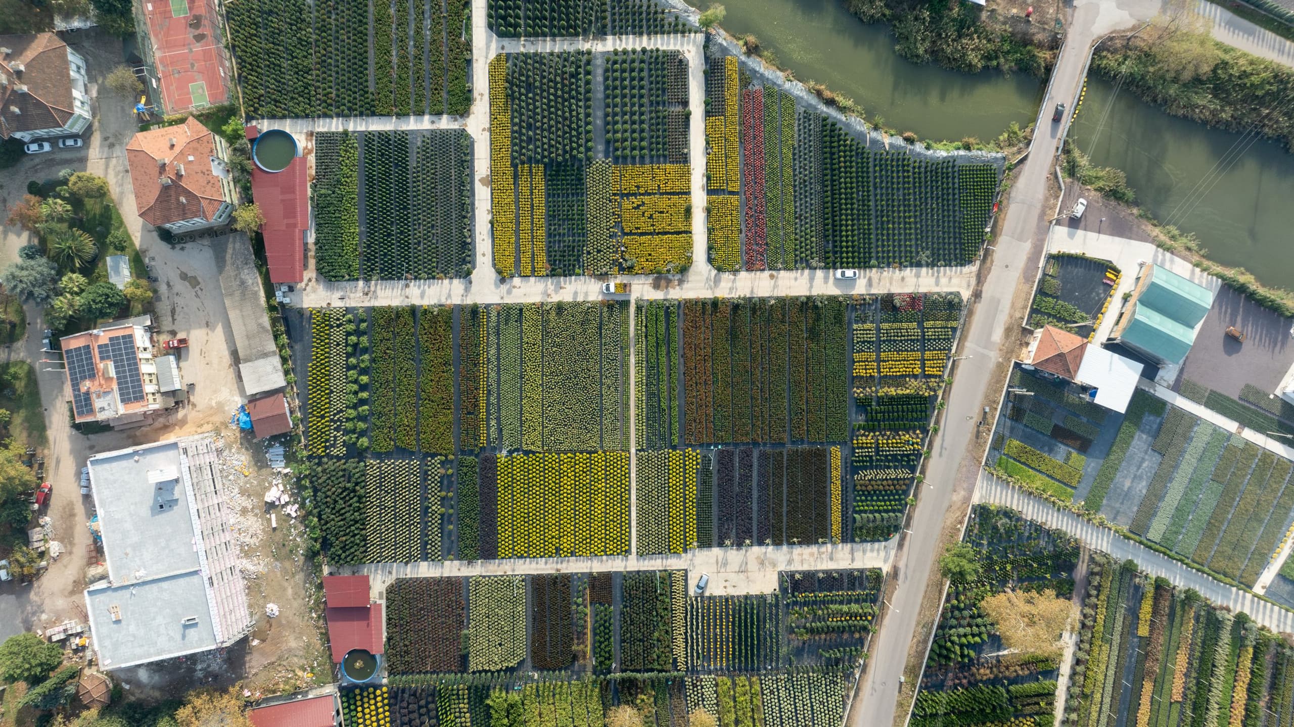 Near-vertical aerial view of cultivated plots at Yalova divided by hard boundaries, with a public road giving frontage down one side, a watercourse along the top and buildings on the parcel edges.