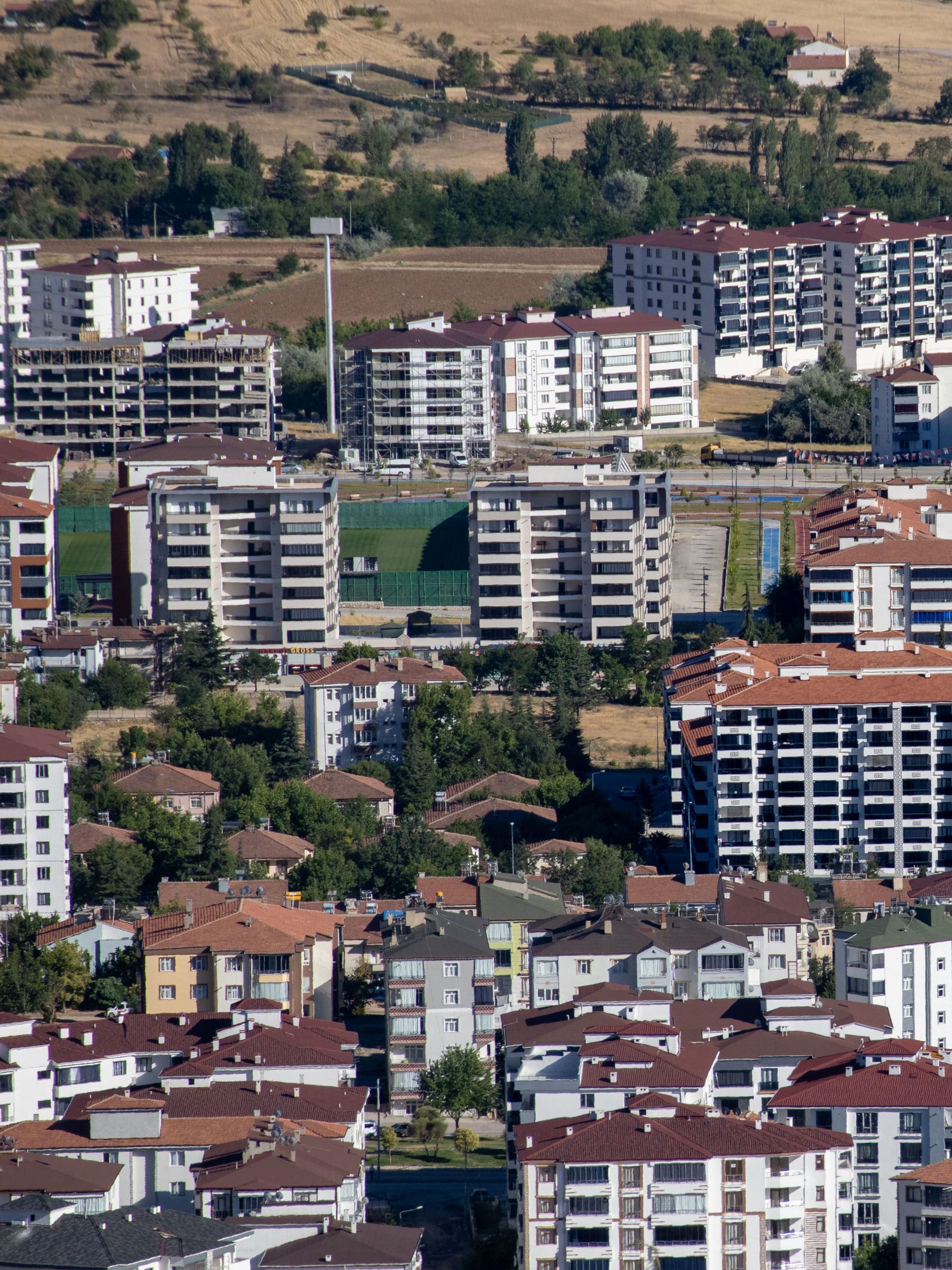 Elâzığ read from height: the last rows of apartment blocks stopping on a hard line against open cultivated parcels, with the road that serves them running along the boundary.